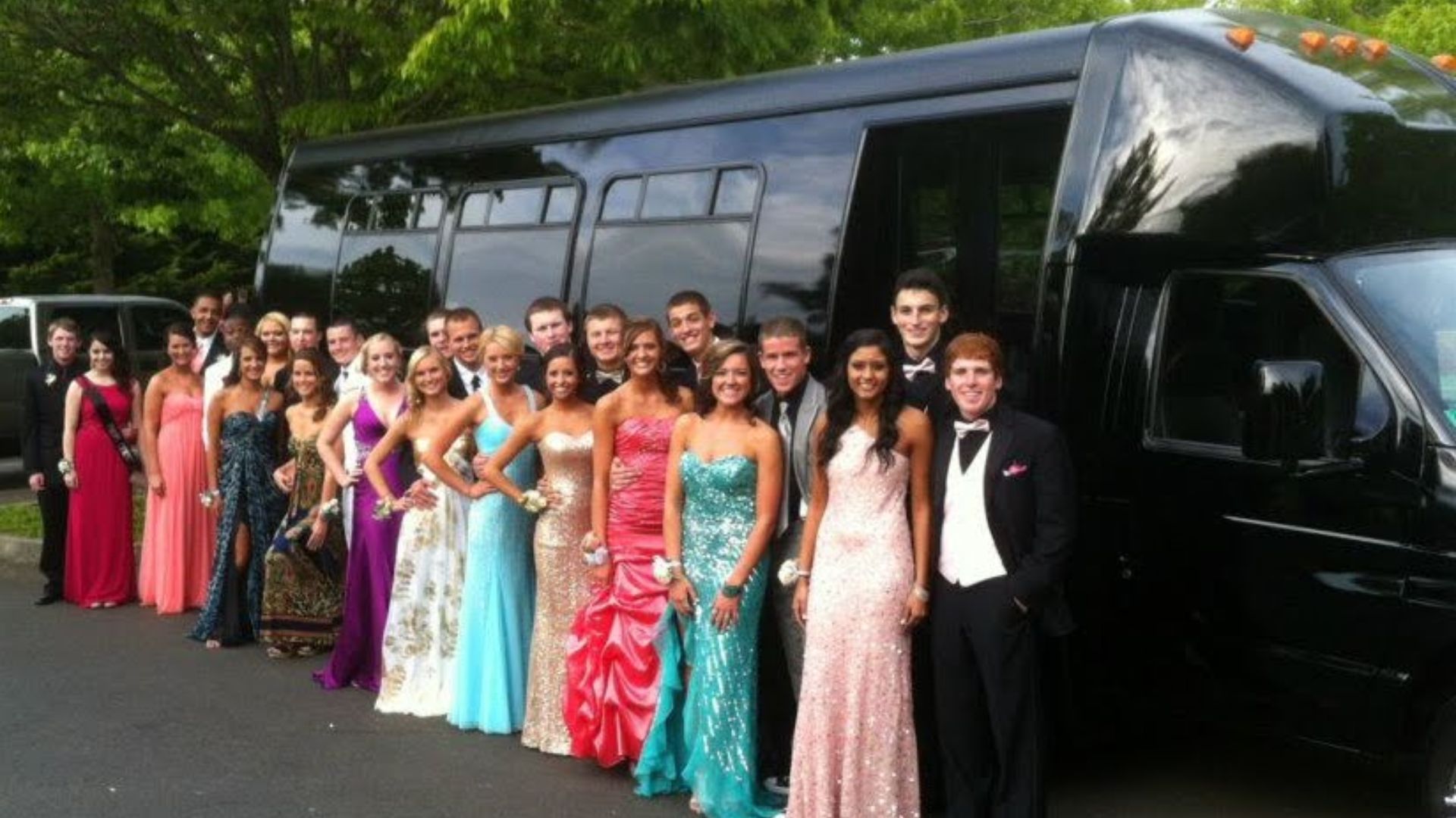 Group of prom goers stand in front of a party bus before board.